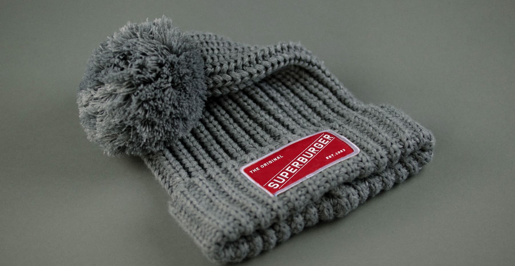 A Superburger-themed grey beanie with a red label on it.